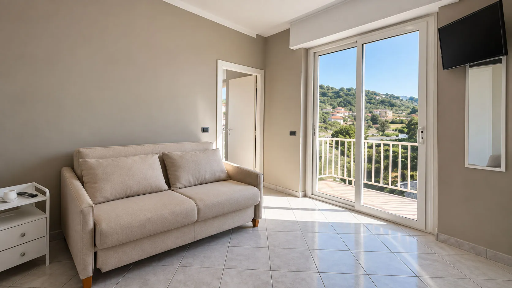 Zona giorno con divano e balcone vista collina in una camera dell'Hotel Sole Mare